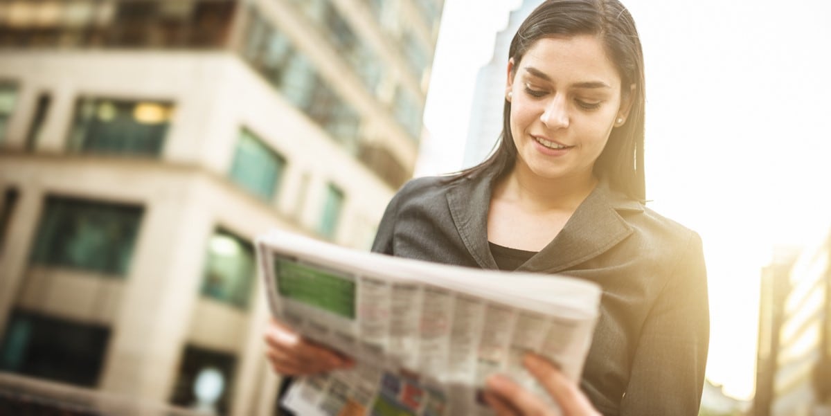 mujer con periodico parada afuera, ciudad