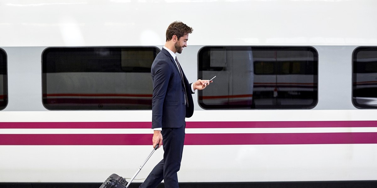 man with luggage looking at phone, standing by train